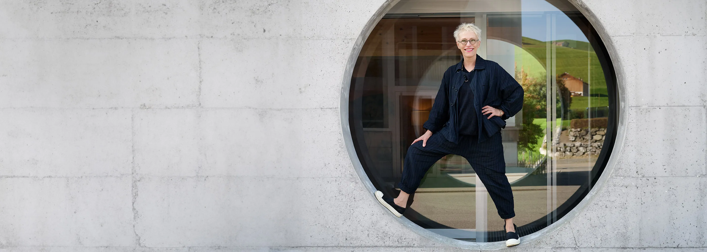 Lächendle Frau steht in Rahmen eines runden Betonfenster