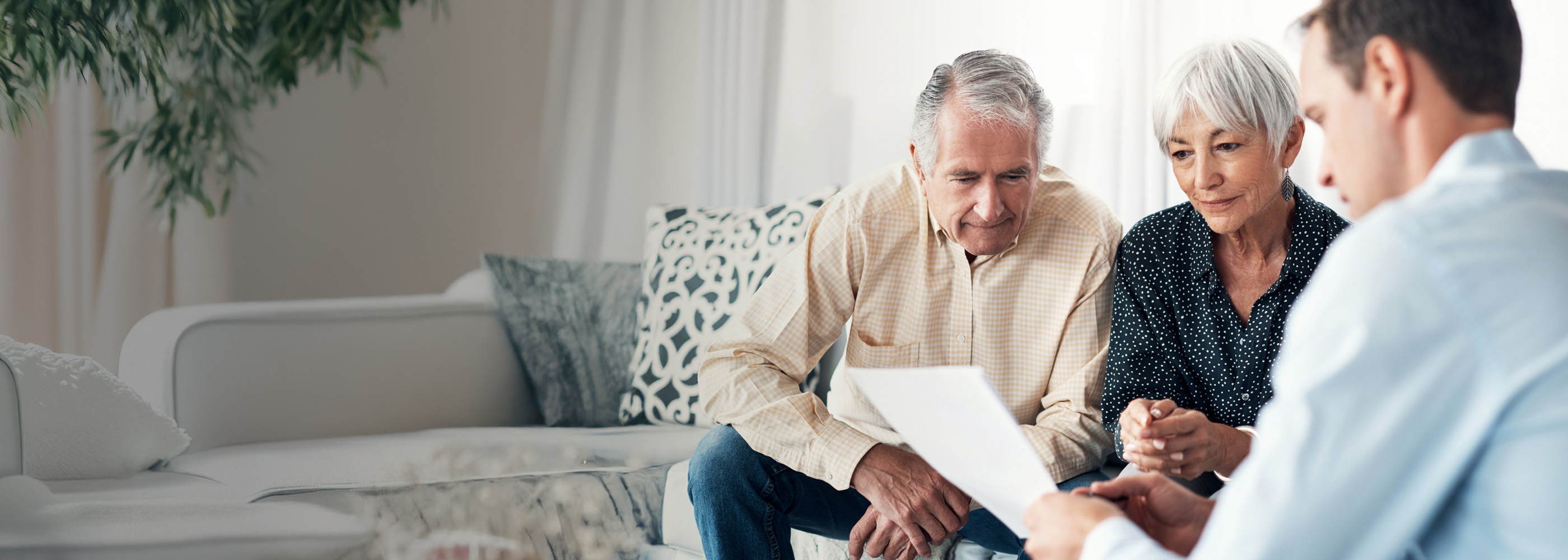 Ein Paar und ein Notar sitzen auf einer Couch und schauen sich das Testament an.